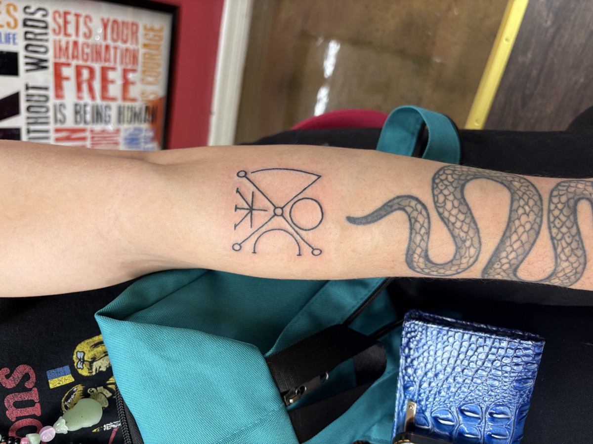 Fine line alchemical sigil symbol tattoo in black on inner forearm