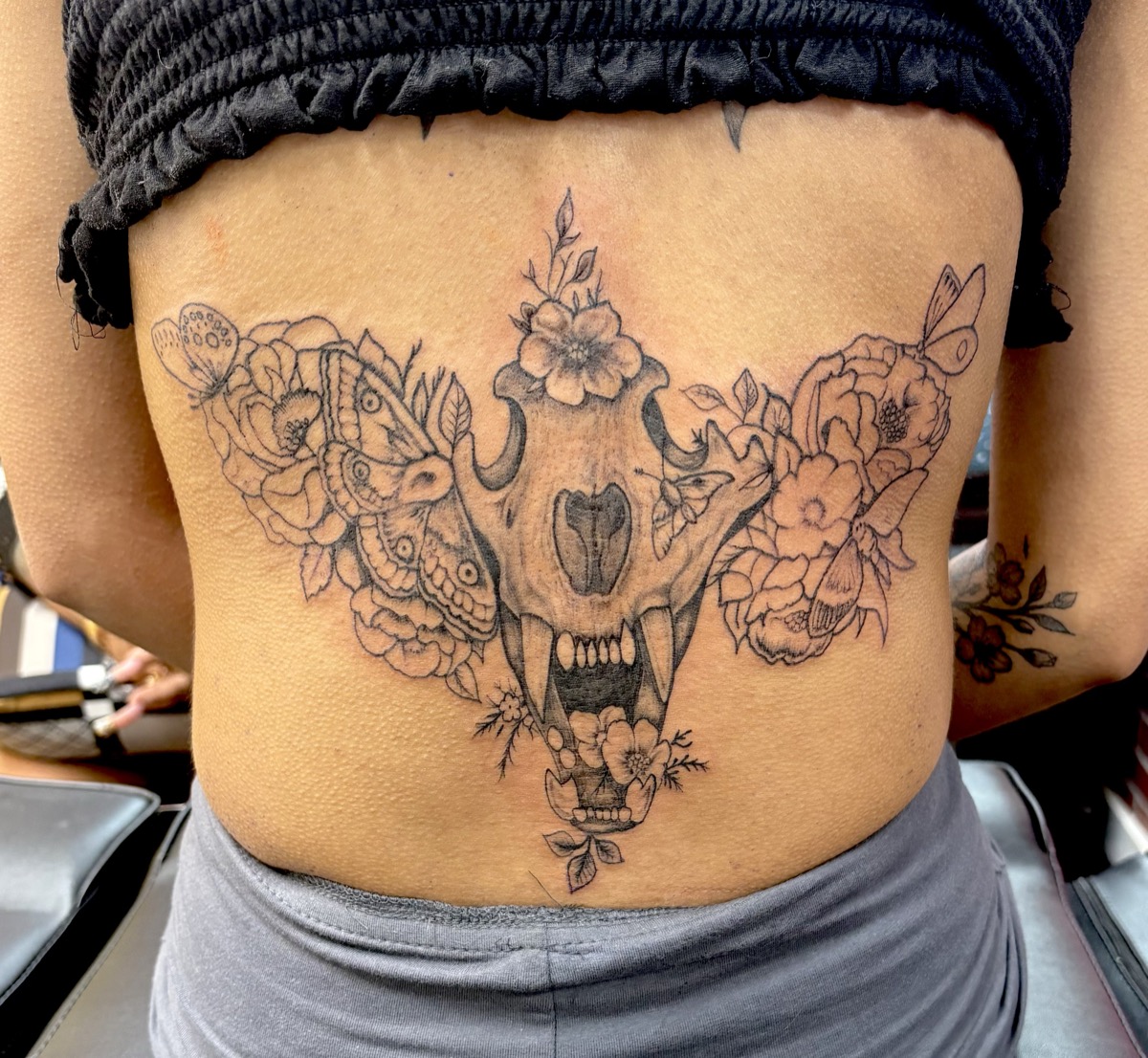 Large cat skull with mandala patterns surrounded by flowers and botanicals on lower back