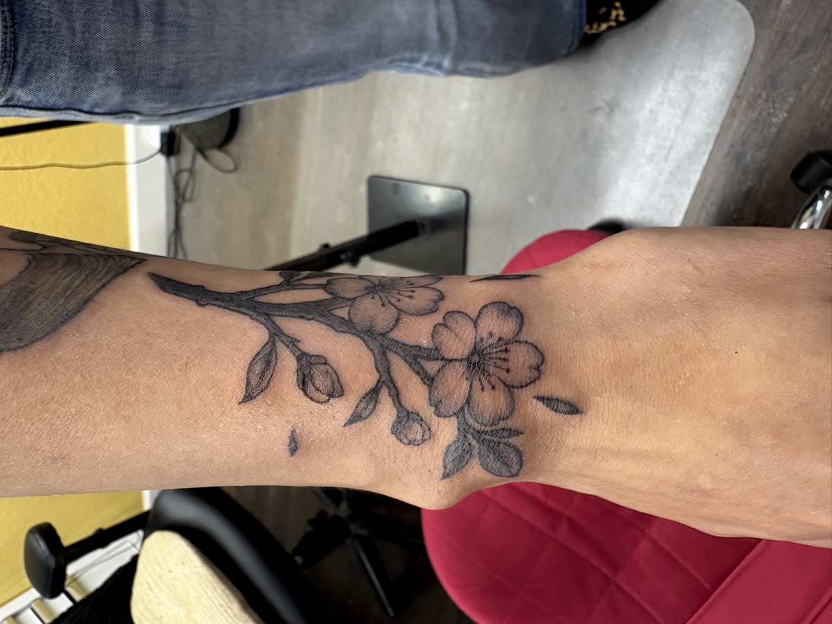 Delicate cherry blossom branch tattoo with flowers and buds on inner forearm