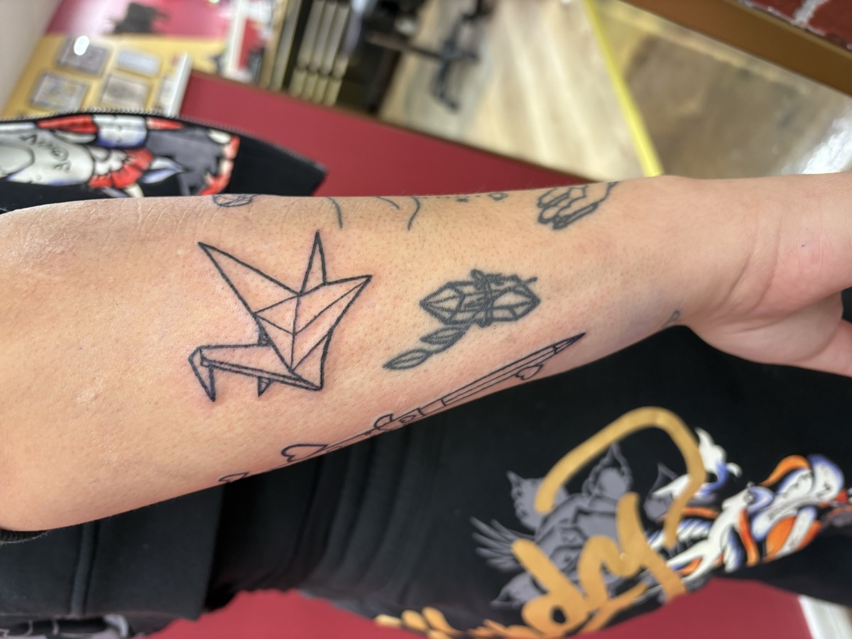 Minimalist geometric origami paper crane tattoo in black linework on forearm