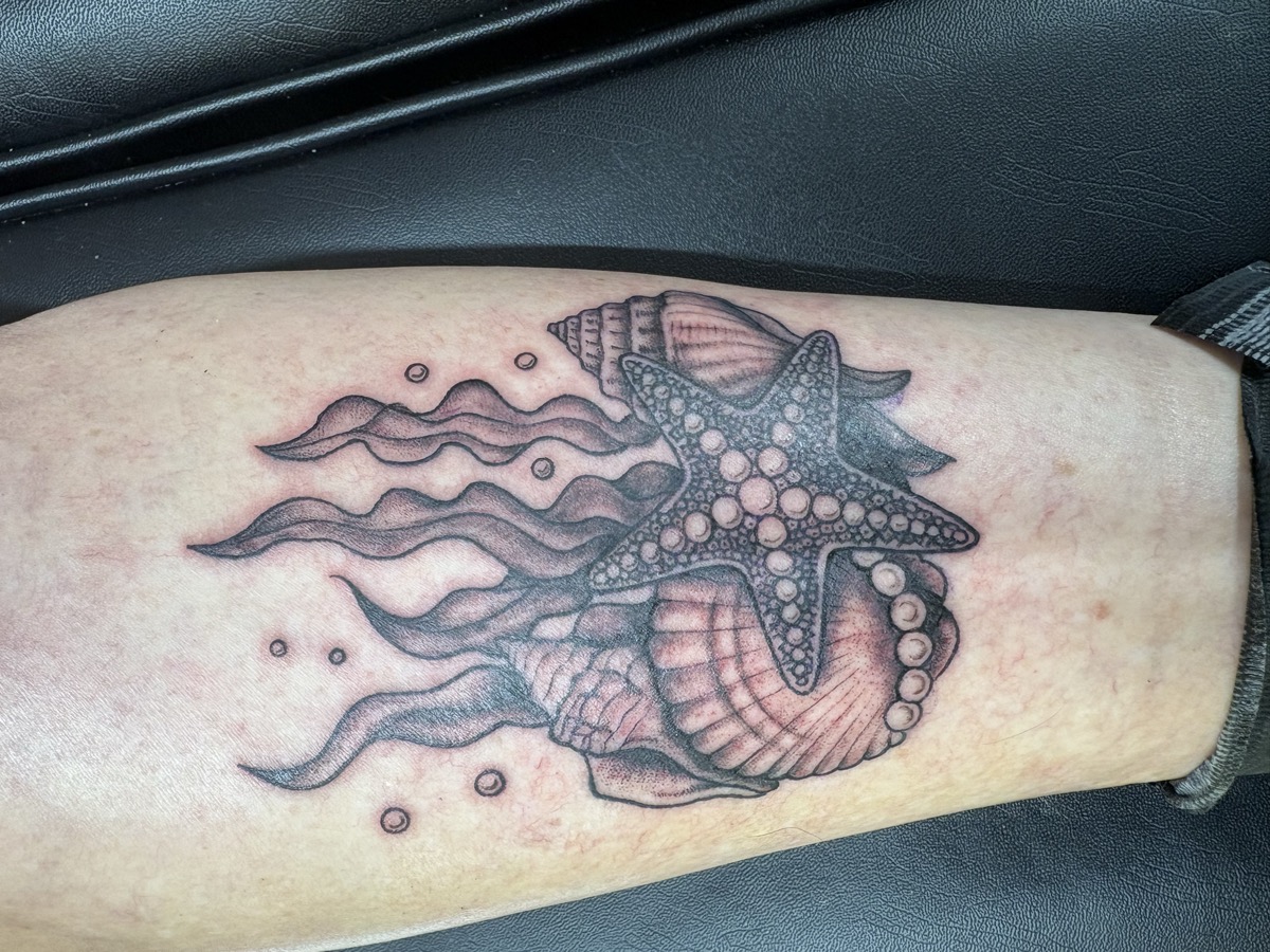 Black and grey seashells, starfish, and ocean waves tattoo with bubbles on calf