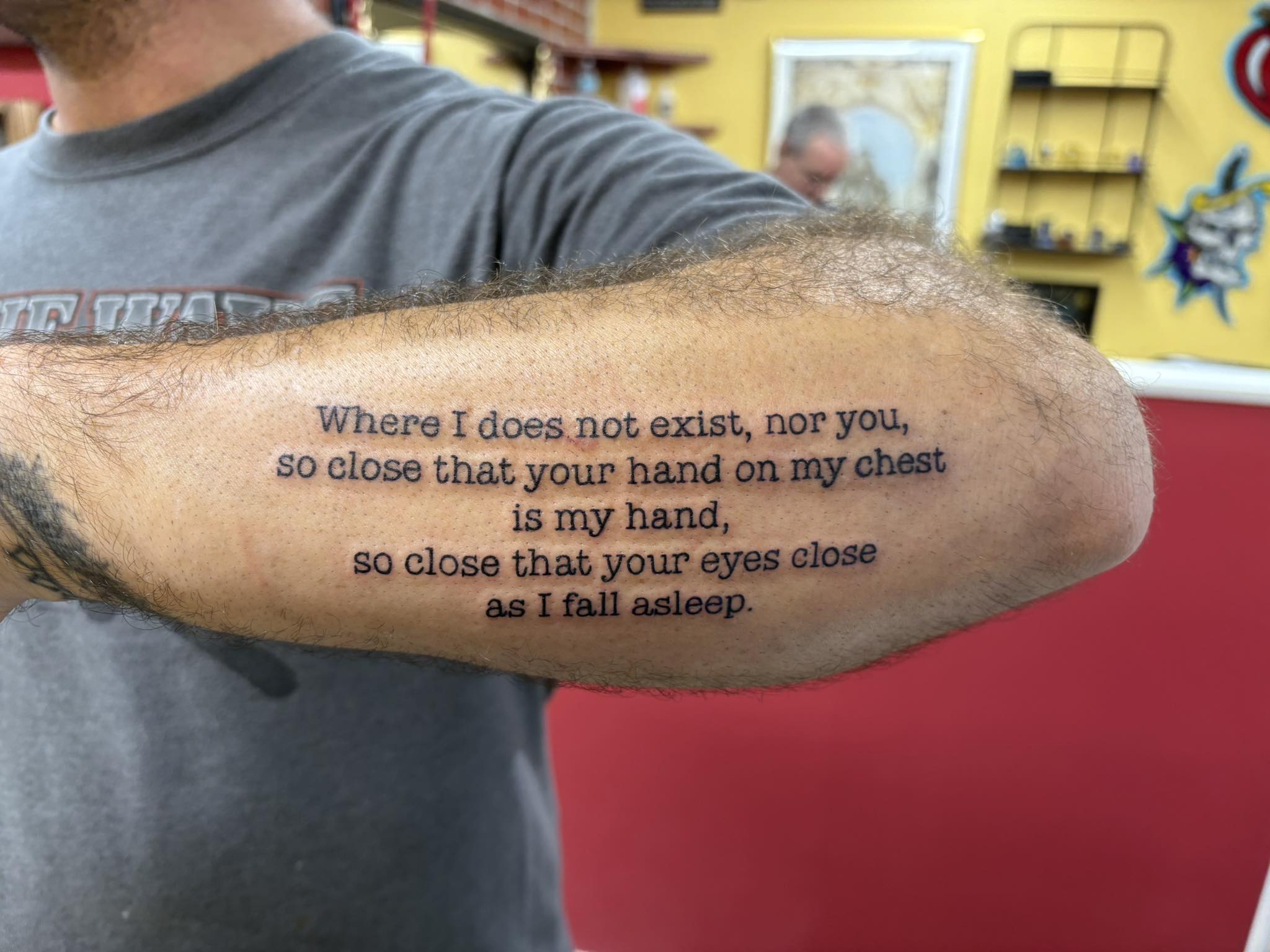 Poetry quote tattoo in bold typewriter font on forearm